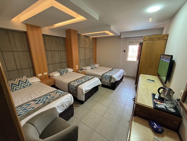 A hotel room with three beds, a TV, a coffee maker, and a small table with glasses and a kettle.