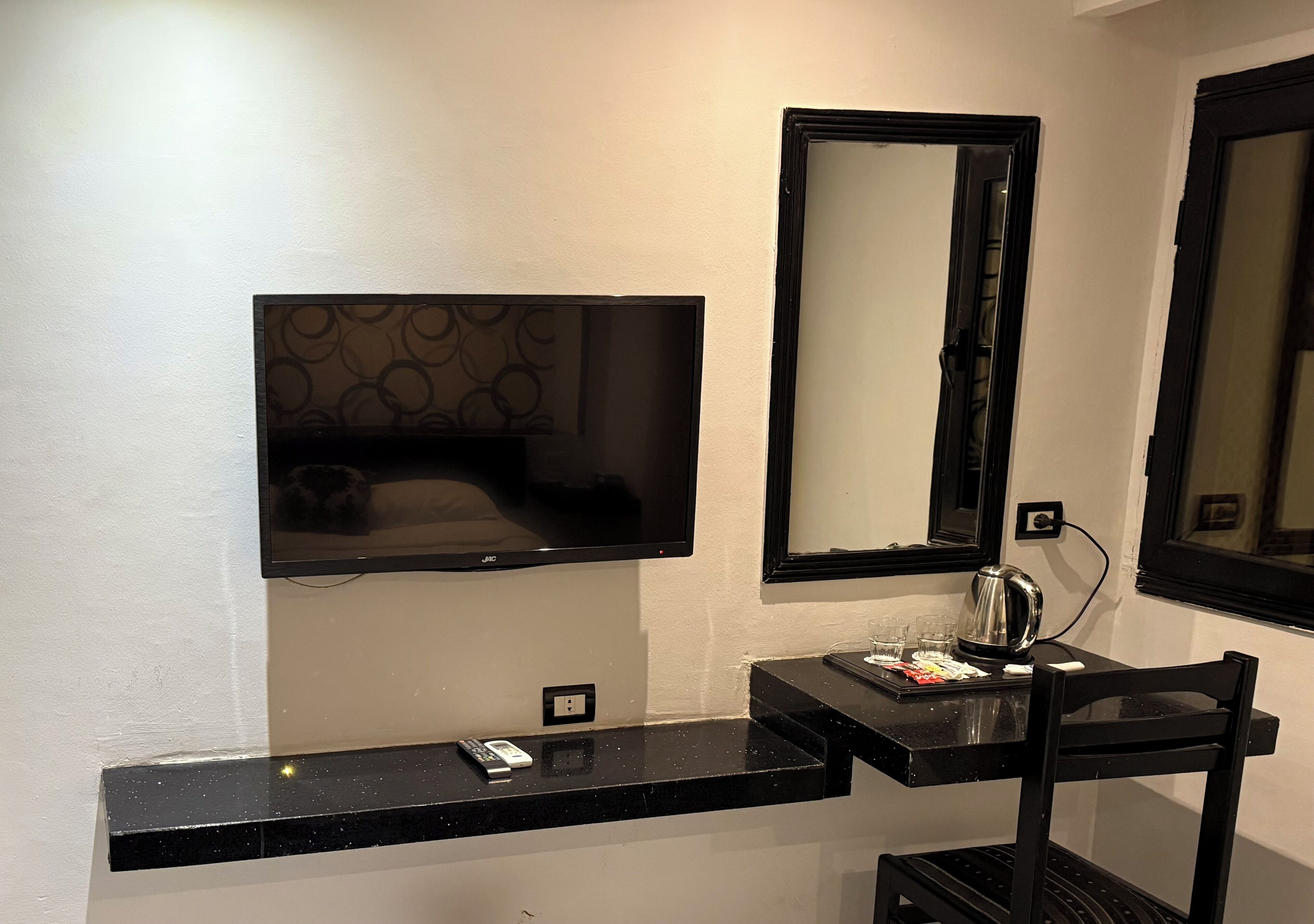 Un baño moderno con un mostrador negro, un espejo, un lavabo y un televisor montado en la pared.