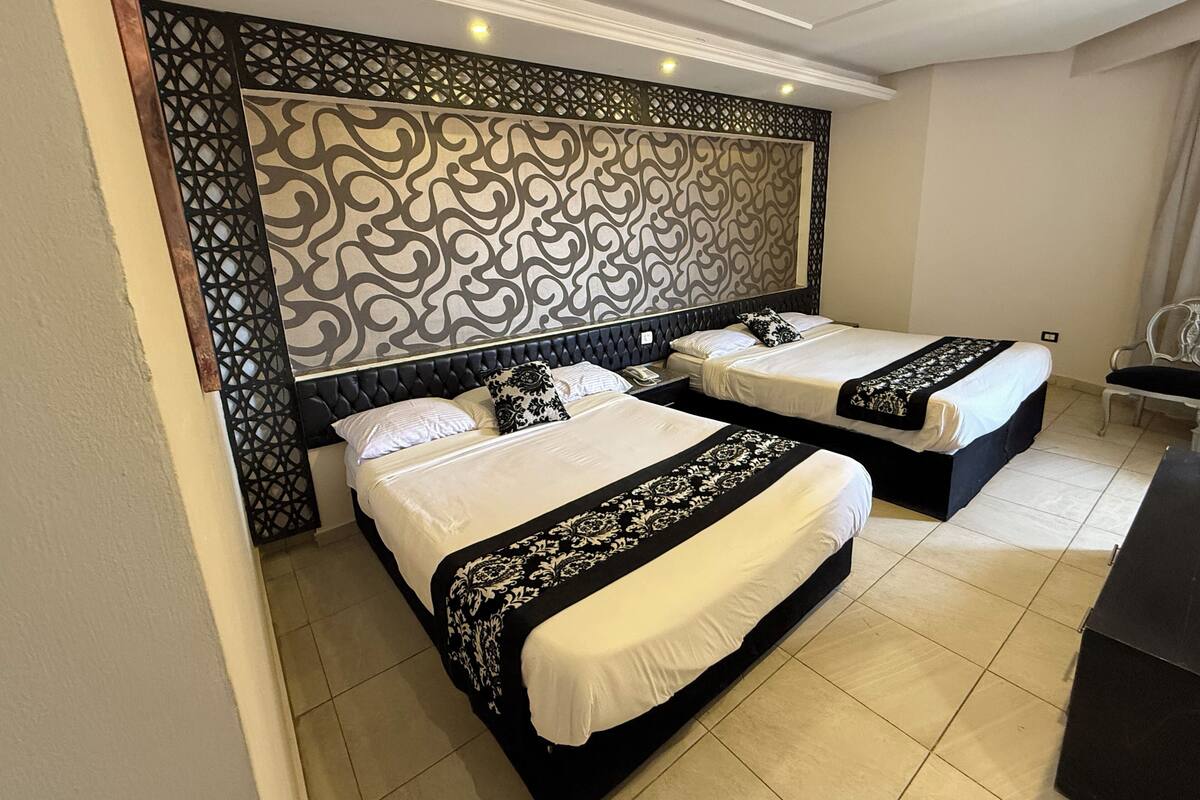 A hotel room with two beds, a decorative headboard, and a chair.