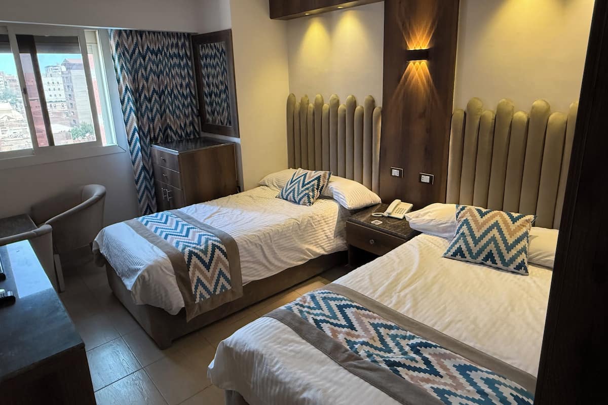 A hotel room with two beds, a desk, a chair, and a window with curtains.