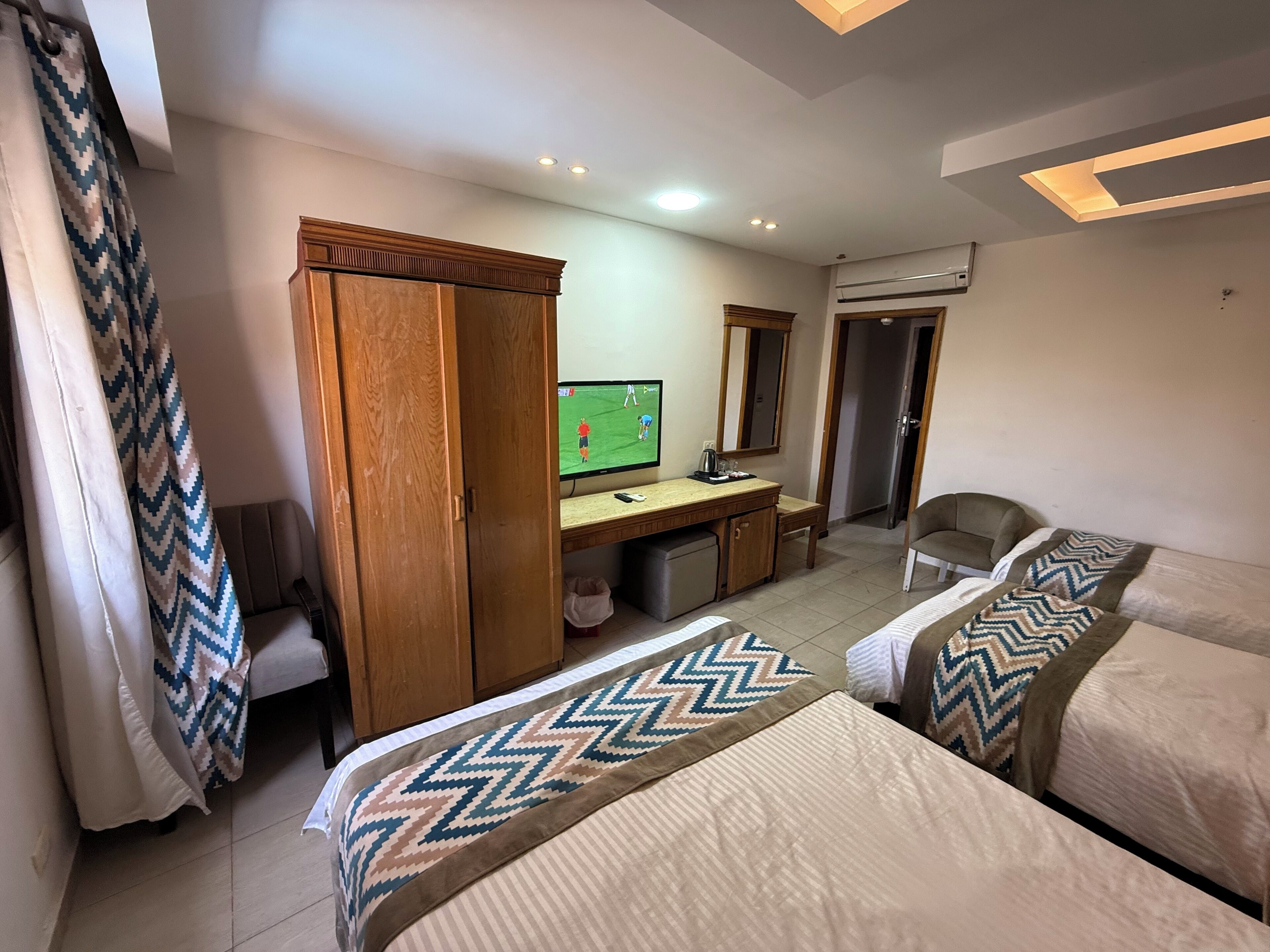Una habitación de hotel con dos camas, un escritorio con televisor, un espejo y un equipo de aire acondicionado.