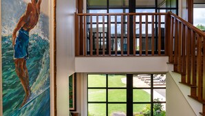 Una escalera con barandilla de madera, un cuadro grande de un surfista y vistas al exterior.