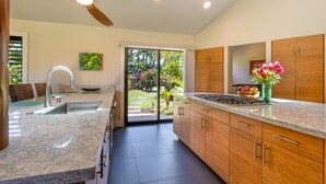 Una cocina moderna con encimera de granito, armarios de madera, ventilador de techo y vistas a un jardín a través de puertas de vidrio.