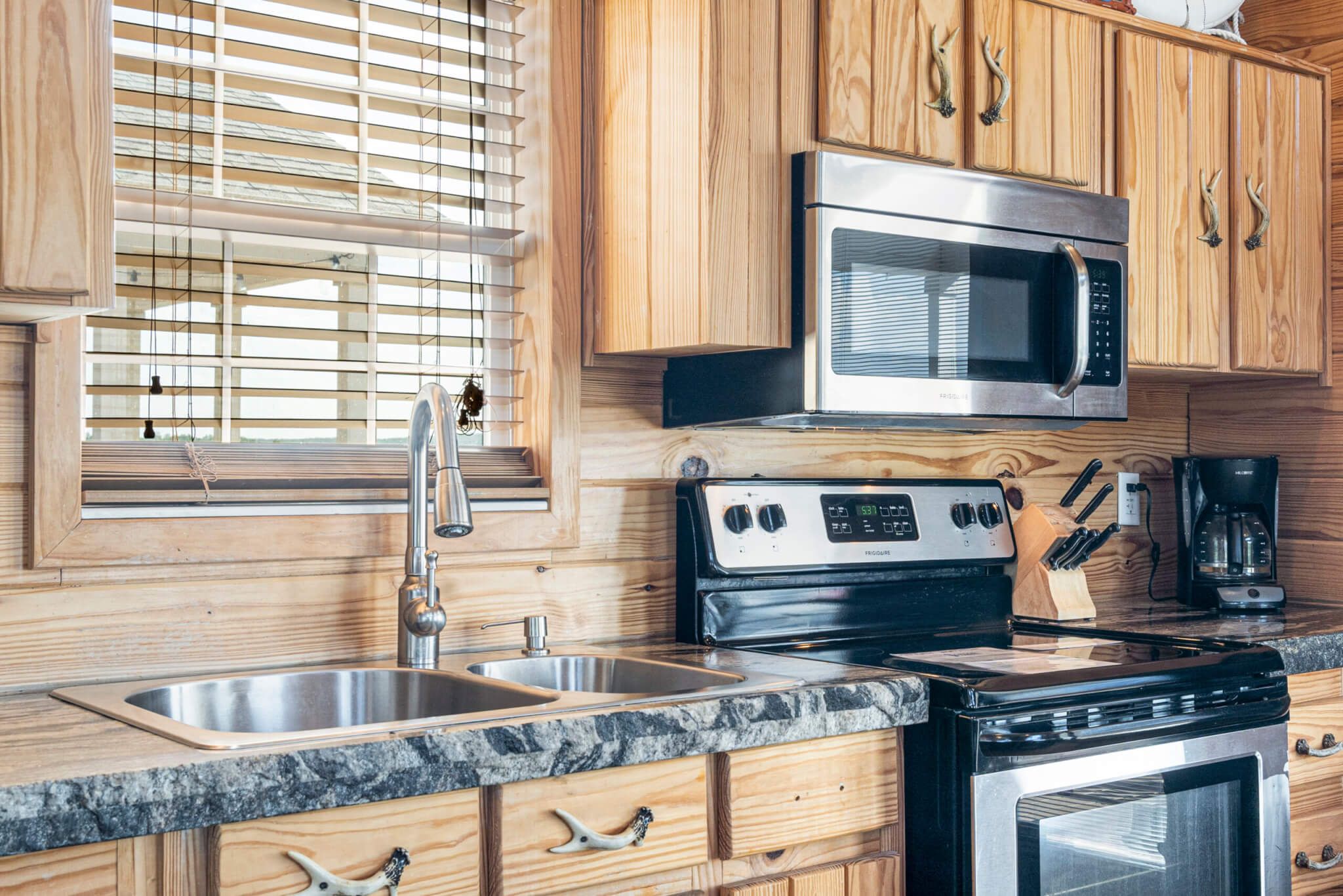 A kitchen with wooden cabinets, a stainless steel sink, a microwave, a stove, and a coffee maker.