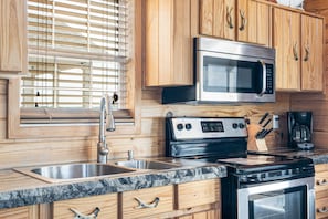 Una cocina con gabinetes de madera, un lavamanos de acero inoxidable, un microondas, una estufa y una cafetera.