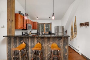 A kitchen with wooden cabinets, a marble island with bar stools, stainless steel appliances, and pendant lighting.