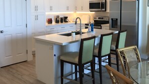Una cocina moderna con armarios blancos, electrodomésticos de acero inoxidable y una isla central con taburetes.