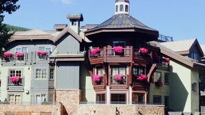 Um hotel de vários andares com fachada de pedra, várias varandas com floreiras e uma estrutura imponente semelhante a uma torre.