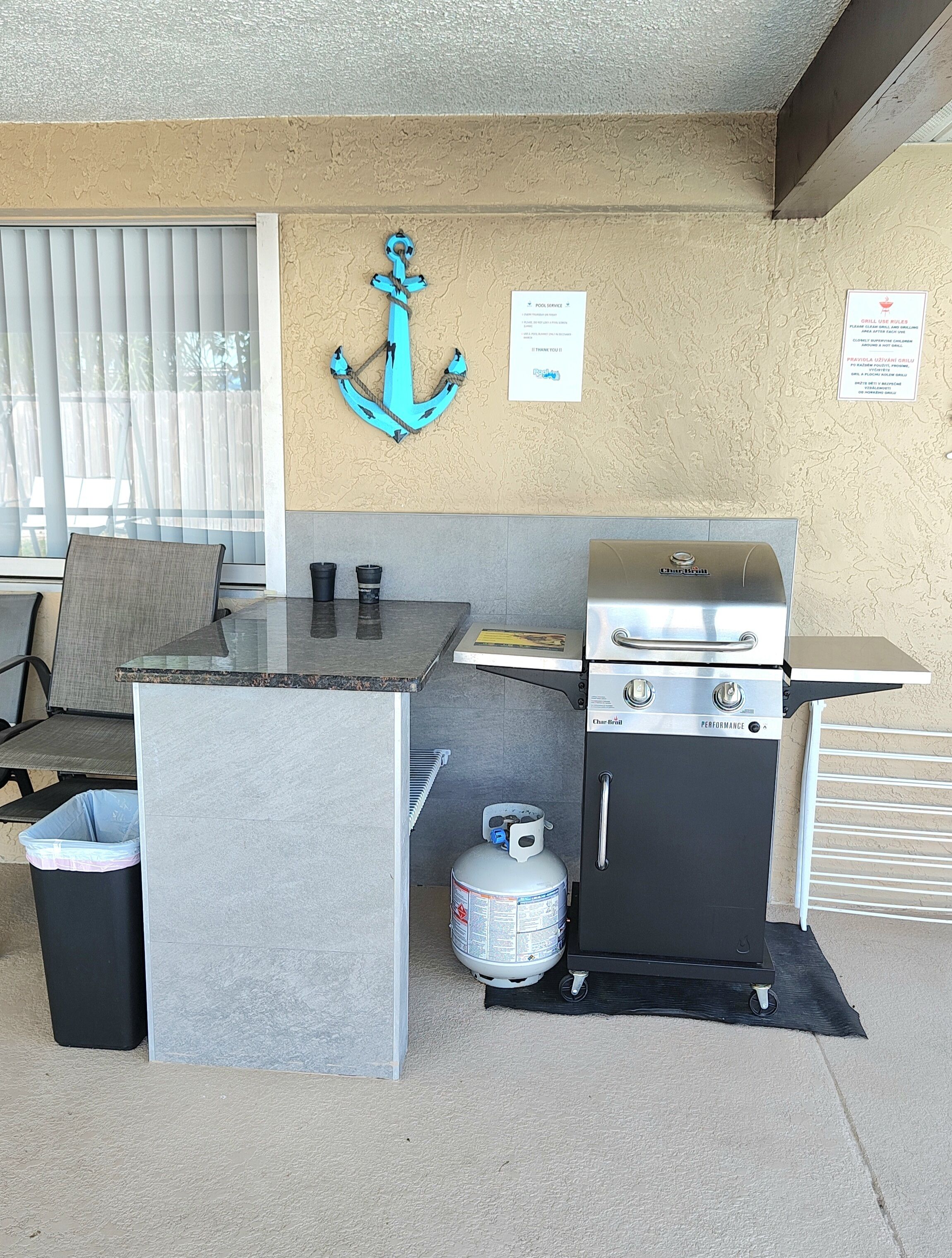 Un espace cuisine extérieur compact comprenant un barbecue, une table avec des chaises, une poubelle et une bouteille de propane.