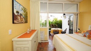 Un dormitorio con cama, una mesita, una silla, un cuadro y vistas al exterior.