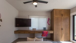 A bedroom with a bed, a desk with a TV, a wardrobe, and a window.