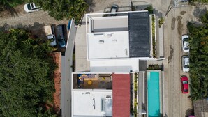 An aerial view of a modern building with a rooftop pool, multiple parking spaces, and surrounding greenery.