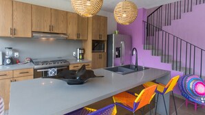 A modern kitchen with wooden cabinets, a stainless steel stove, and a large island with colorful chairs.