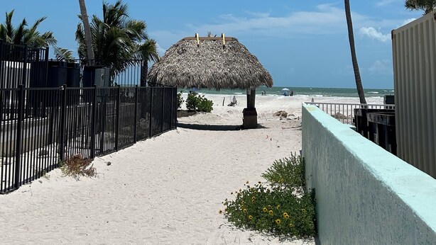A beach pathway with a thatched-roof structure, palm trees, and a sandy beach. - Welcome to Santa Maria 310, a little piece of Paradise! (Fort Myers Beach)
