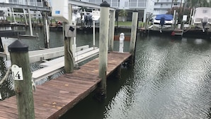 A wooden dock extending into calm water, with a building and boats in the background. - Welcome to Santa Maria 310, a little piece of Paradise! (Fort Myers Beach)