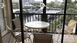 A balcony with a round table and four chairs, overlooking a marina with boats and buildings. - Welcome to Santa Maria 310, a little piece of Paradise! (Fort Myers Beach)