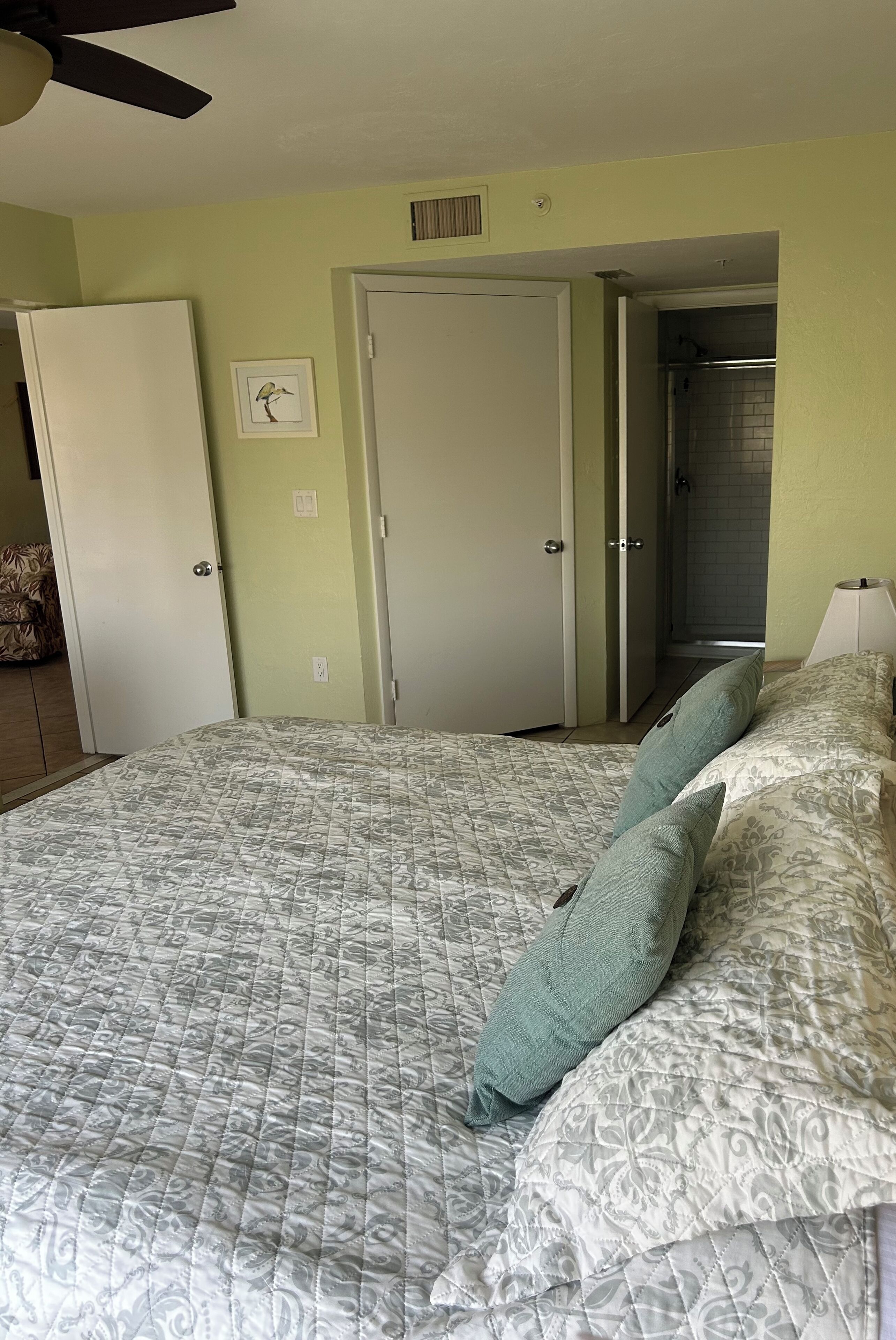A bedroom with a bed, two pillows, a ceiling fan, and a door leading to a bathroom.