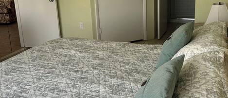 A bedroom with a bed, two pillows, a ceiling fan, and a door leading to a bathroom.