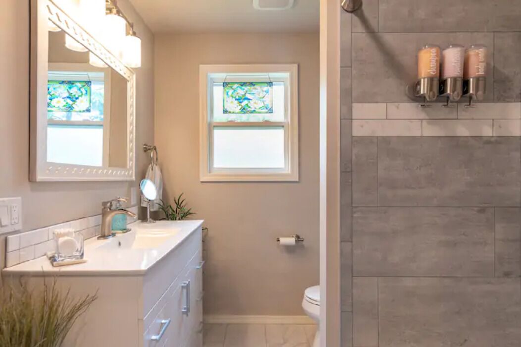 A bathroom with a white vanity, a large mirror, a stained glass window, and a shower area with candles.