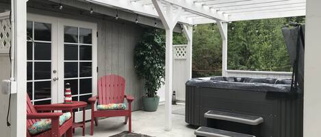 Un patio couvert comprenant un jacuzzi, deux fauteuils Adirondack rouges, une plante en pot et un tapis à motifs.