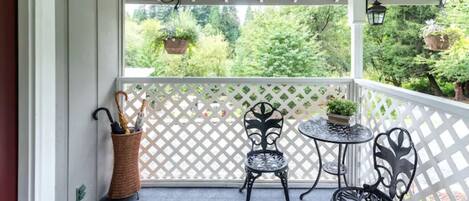 A covered balcony with two metal chairs, a small round table, and a wicker basket with an umbrella.