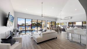 Ein modernes Wohnzimmer mit großem Fenster, Pool, einer Couch und einer Küchenzeile.