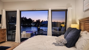 Ein Schlafzimmer mit einem großen Bett, Blick auf einen Pool und einem Balkon mit Sitzgelegenheit.