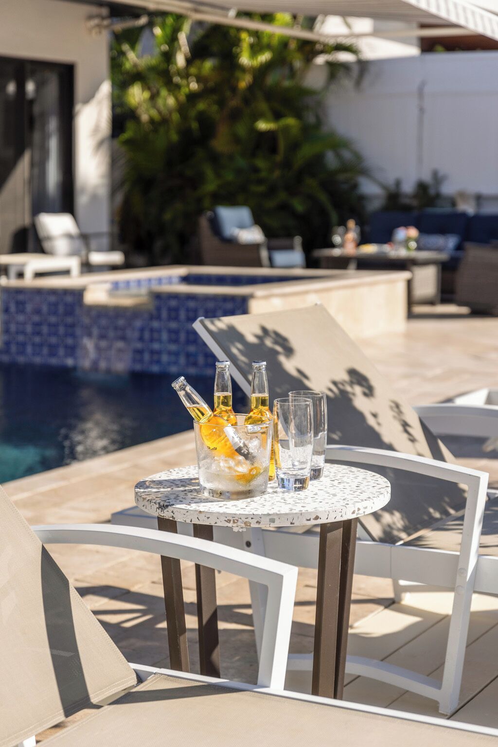 A poolside table with drinks and glasses, surrounded by lounge chairs and a pool.