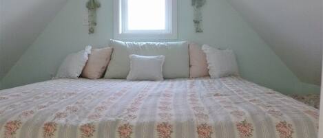Un dormitorio con techo inclinado, una ventana y una cama con ropa de cama estampada con motivos florales.