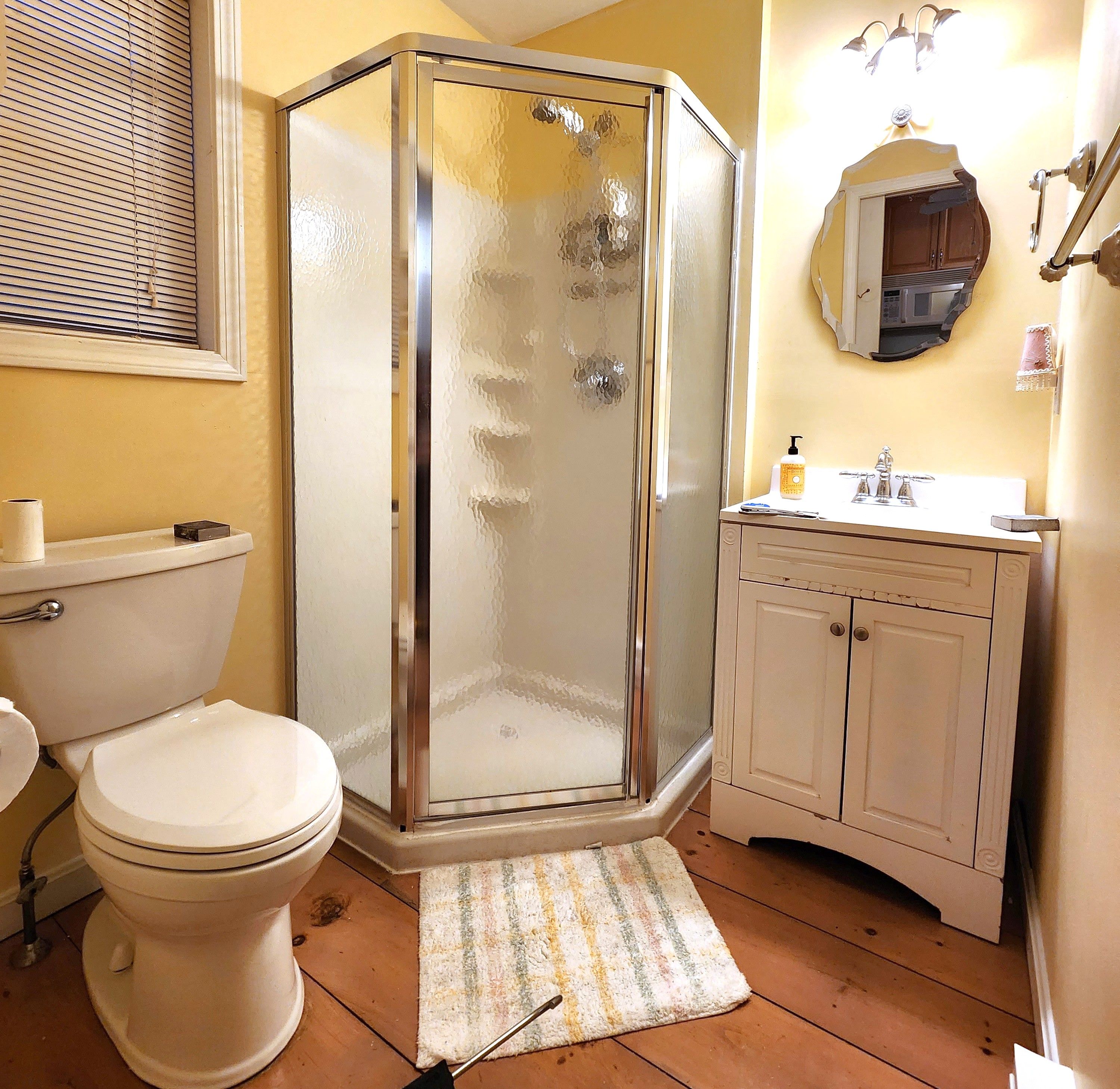 A bathroom with a toilet, a shower enclosure, a sink, and a mirror.