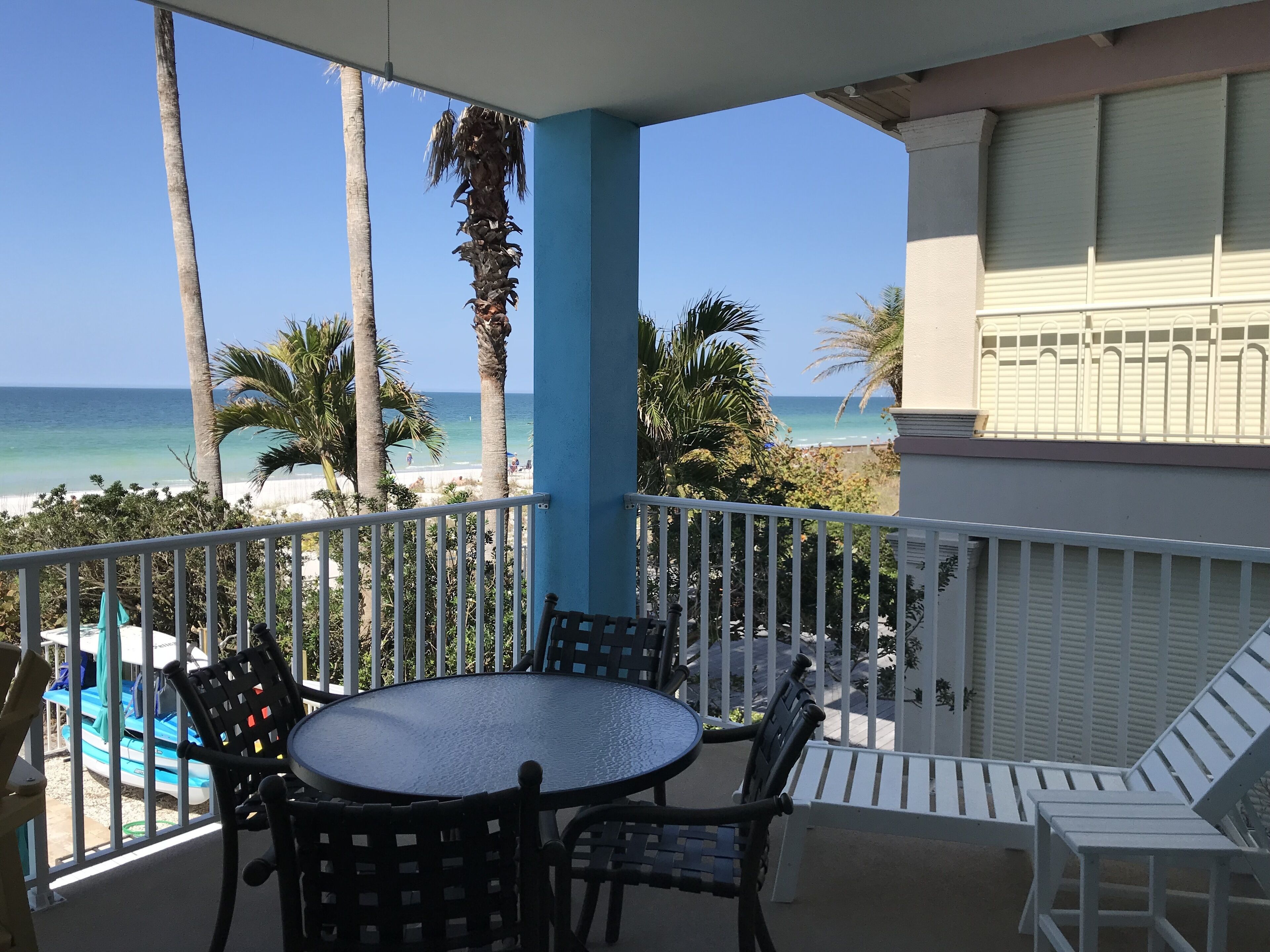 Un balcon avec une table ronde et des chaises, donnant sur une plage bordée de palmiers et sur l’océan.