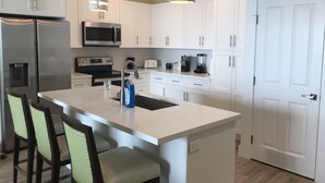 A modern kitchen with white cabinets, stainless steel appliances, a central island with bar stools, and pendant lighting. - NEW Beachfront Condo, 2/2, Balcony, Heated Pool, INDIAN ROCKS BCH, Unit 303 (Indian Rocks Beach)