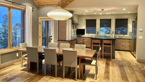 Eine moderne Küche mit Holzboden, einem Essbereich mit Tisch und Stühlen sowie großen Fenstern mit Blick ins Freie.