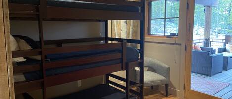 Una cama litera con ropa de cama azul, un sillón gris y una terraza de madera con mobiliario exterior.