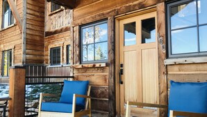 Eine Holzhütte mit Veranda, zwei blaue Sitzkissen und einer Tür mit einer Nummernschild.
