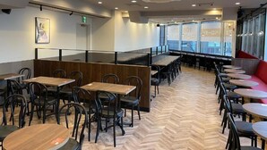 A restaurant with a long counter, multiple tables, and chairs. There are windows along one side, and a door is visible in the background. - APA Hotel Ueno Inaricho Ekikita (Tokyo)