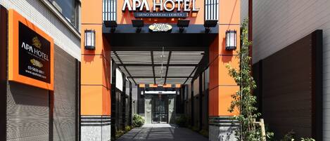 La entrada del Hotel APA, con un diseño moderno, que incluye un vestíbulo cubierto y señalización clara.