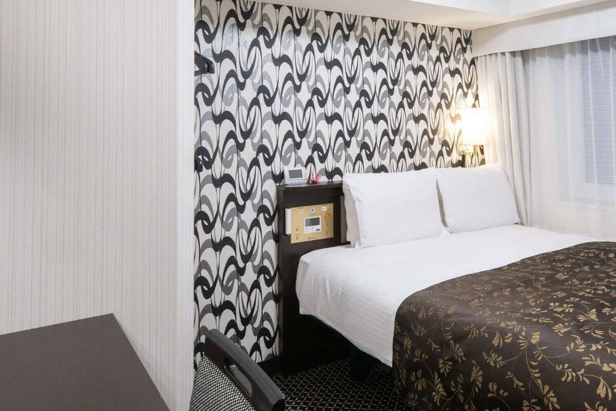 Habitación de hotel con cama, escritorio, silla, mesita de noche con lámpara y pared con diseño.