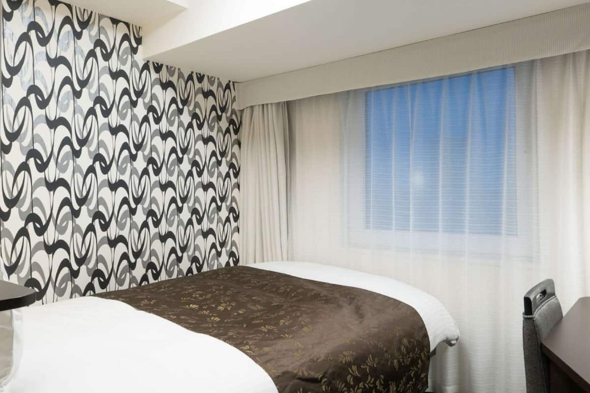 Una habitación de hotel con una cama grande, una mesita y una ventana con cortinas.