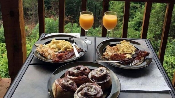 A table with breakfast plates, two glasses of orange juice, and cinnamon rolls on a balcony with a forest view. - OPEN 10/25-30, 11/8-11, 14-25 Knight of My Dreams,Secluded,Amazing View, 1 level (Sevierville)