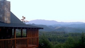 A wooden cabin with a stone chimney, a balcony, and a view of a forested valley and distant mountains. - OPEN 10/25-30, 11/8-11, 14-25 Knight of My Dreams,Secluded,Amazing View, 1 level (Sevierville)