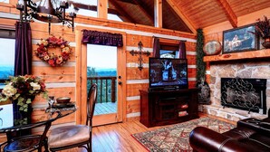 A wooden cabin interior with a fireplace, television, and a dining area with a view. - OPEN 10/25-30, 11/8-11, 14-25 Knight of My Dreams,Secluded,Amazing View, 1 level (Sevierville)
