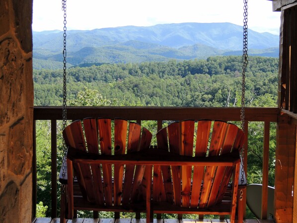 A wooden swing chair on a balcony overlooking a forested mountain range. - Avail 10/2-6, 25-30, 11/8-30 Knight of My Dreams, Secluded, Amazing View,1 level (Sevierville)