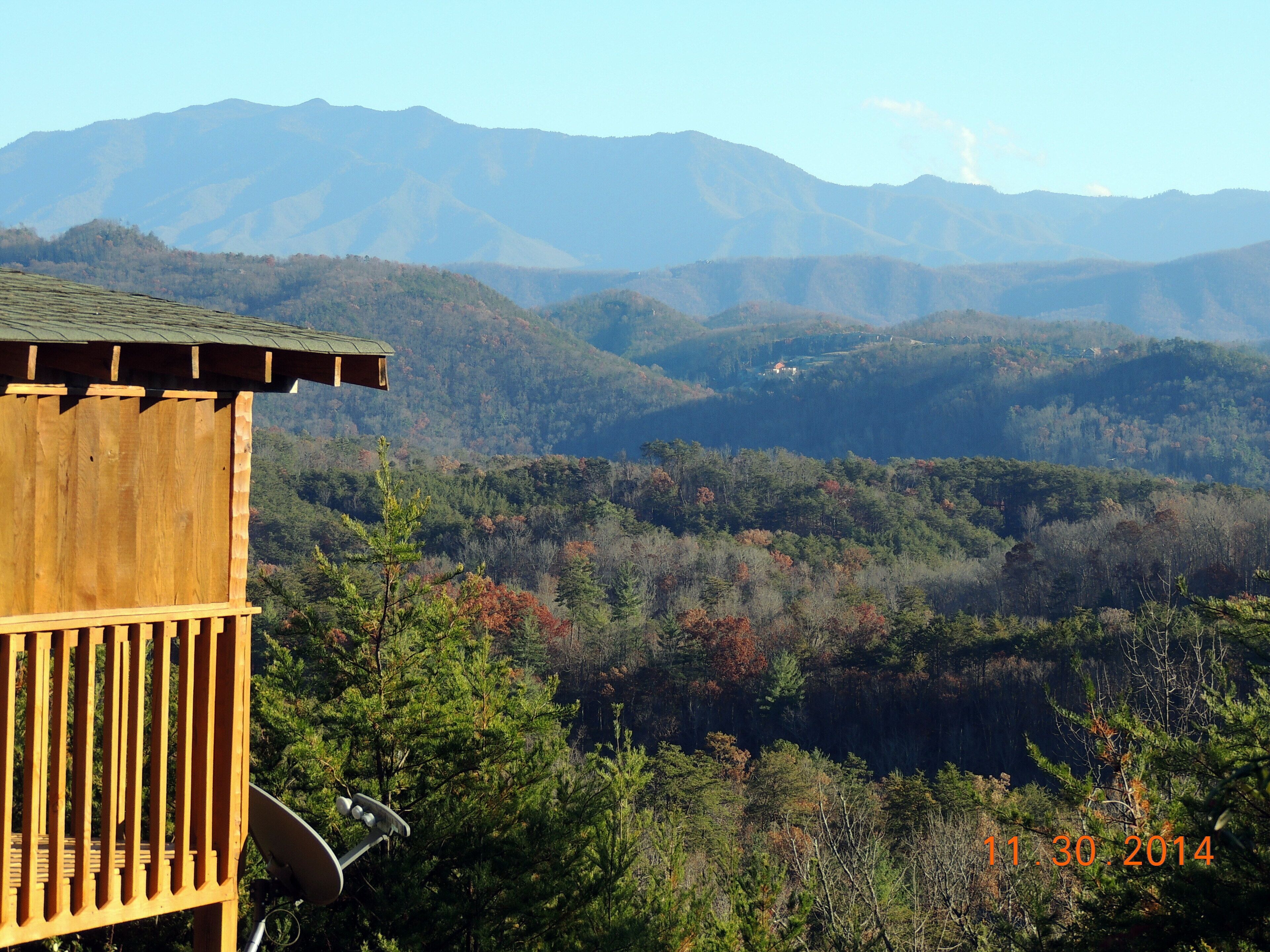 A wooden cabin with a satellite dish, surrounded by dense forest and mountains.