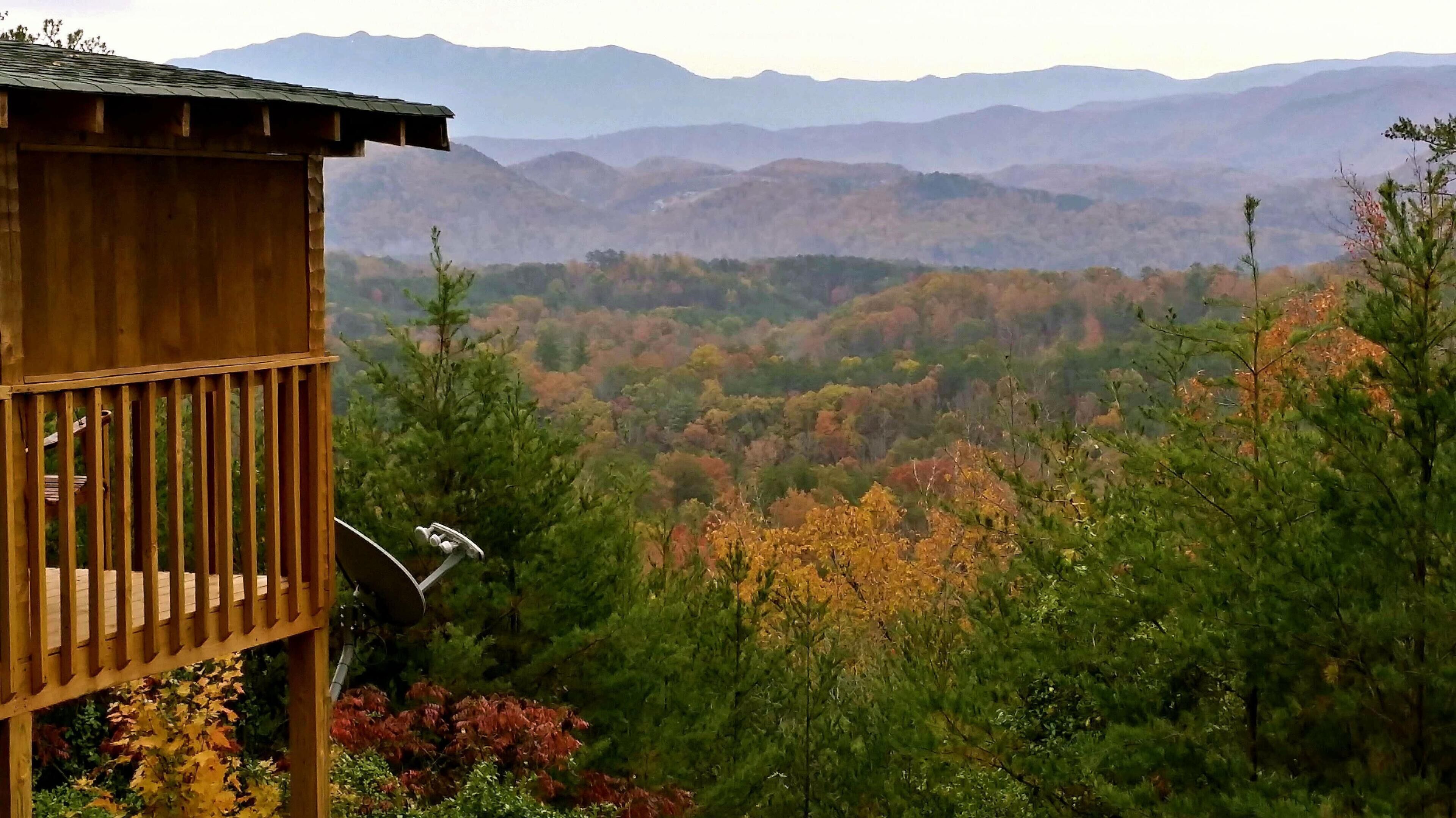 A wooden cabin with a satellite dish, surrounded by autumn foliage and mountains in the background.