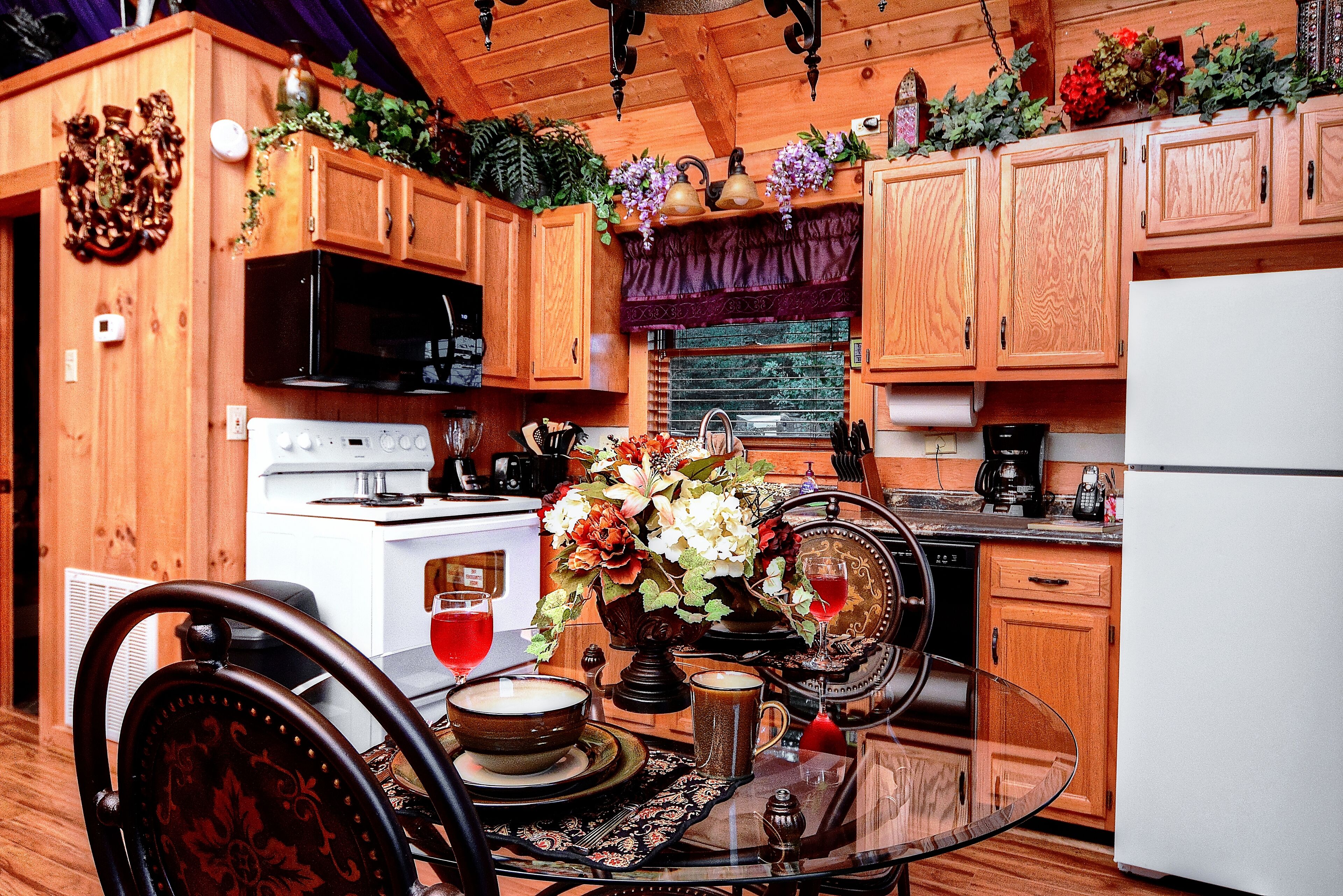 A wooden kitchen with a stove, microwave, and cabinets. There is a dining table with chairs and a vase of flowers.