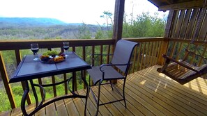 A wooden deck with a table set for a meal, a chair, and a hanging chair. - Avail 10/2-6, 25-30, 11/8-30 Knight of My Dreams, Secluded, Amazing View,1 level (Sevierville)