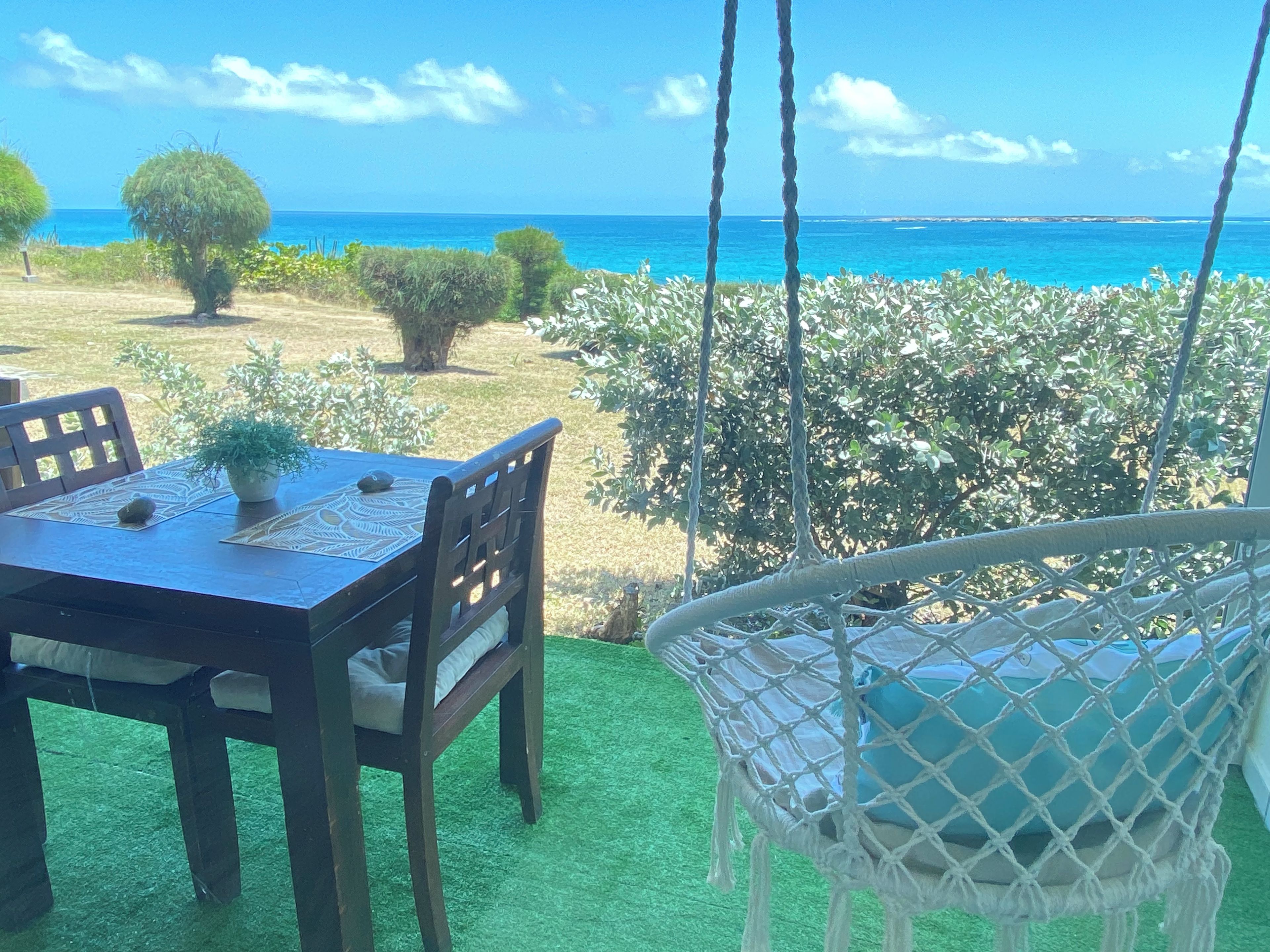 A dining area with a table and chairs, a hanging chair, and a view of the sea.