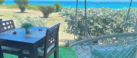 A dining area with a table and chairs, a hanging chair, and a view of the sea.
