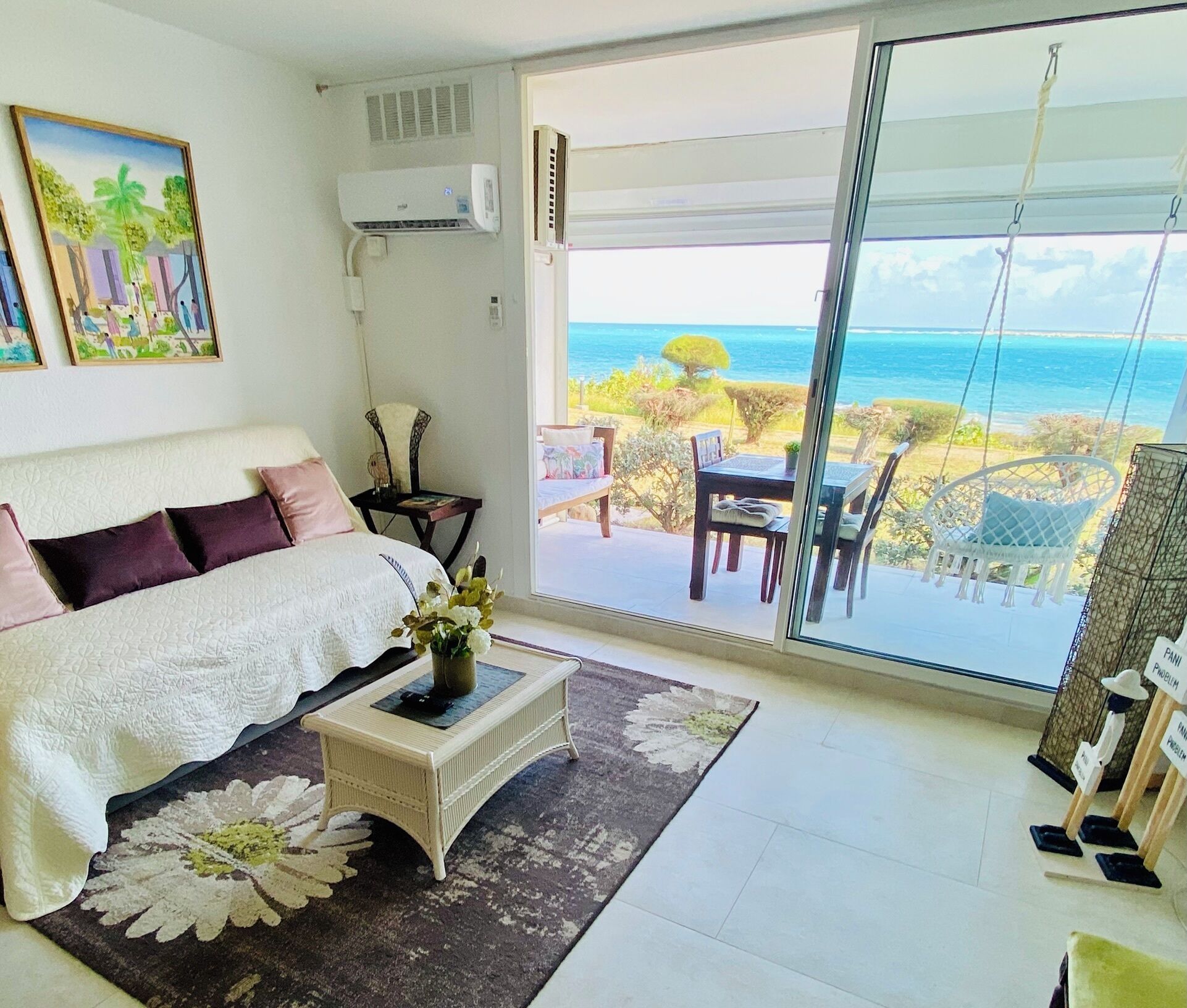 A bedroom with a large bed, a bedside table with a vase, and a view of the ocean through a sliding glass door.